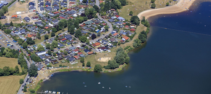 Luftaufnahme eines Wohnviertels an einem See mit Sandstrand und mehreren Booten auf dem Wasser.